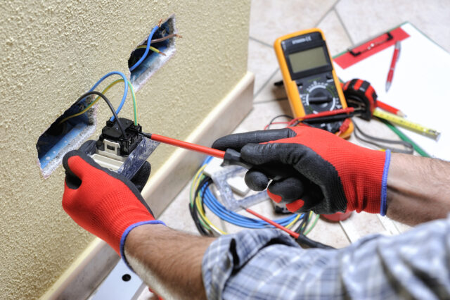 Electrician technician at work blocks the cable between the clamps of a socket in a residential electrical installation