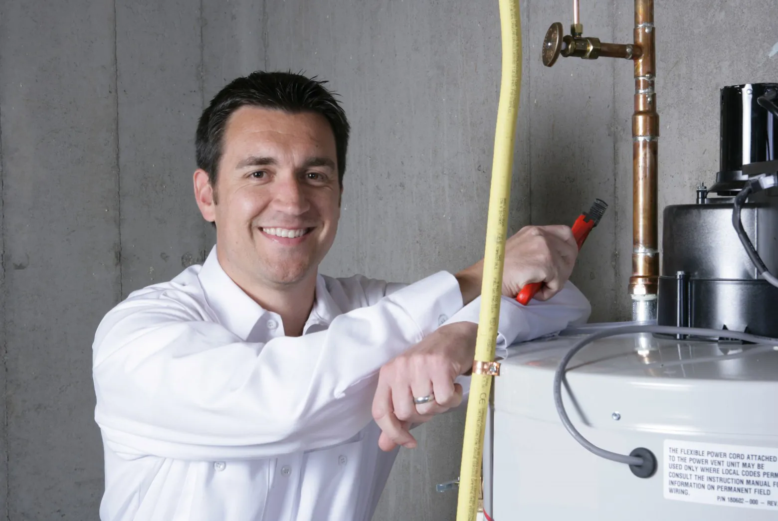 A technician leaning his arms against a power vent water heater, smiling at camera.